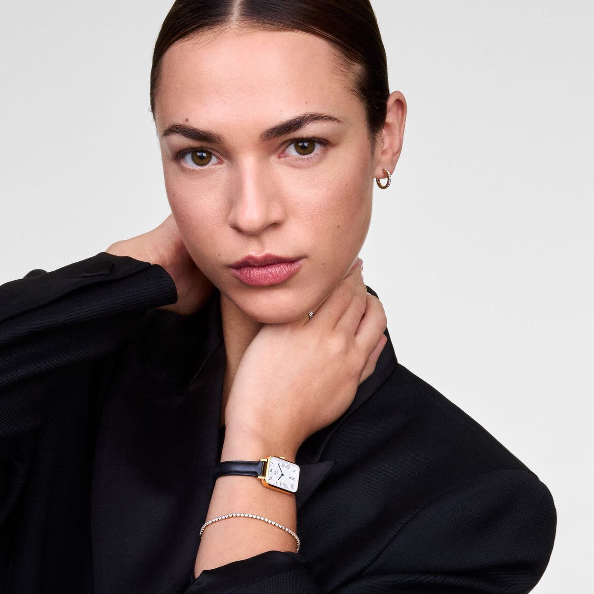 Model wearing the Quadro Roman Numerals Date Sheffield Gold watch, featuring a rectangular gold case, white dial, and black leather strap.