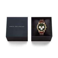 Daniel Wellington Iconic Chronograph St Mawes watch with a gold case, emerald green panda dial, and brown leather strap, shown inside its black brand box.