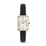 Daniel Wellington Quadro Roman Numerals Date watch with a rose gold rectangular case, textured white dial with blue hands, and a black Sheffield leather strap.