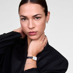 Model wearing the Quadro Roman Numerals Date Sheffield Gold watch, featuring a rectangular gold case, white dial, and black leather strap.