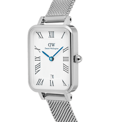 Angled close-up of the Daniel Wellington Quadro Sterling watch, showing the rectangular white dial with Roman numerals, vibrant blue hands, date window, and silver mesh strap.
